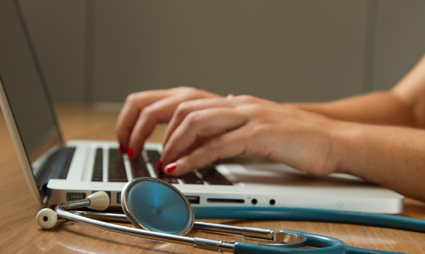Enable Real-time SMS Dialogue - woman's hands on laptop next to stethoscope